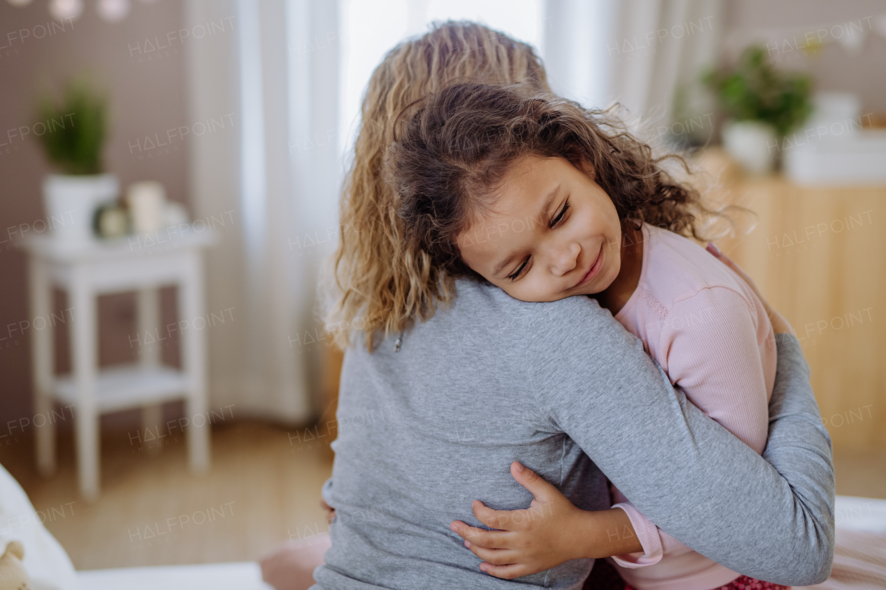 A happy mother with her little daughter hugging together on bed at home.