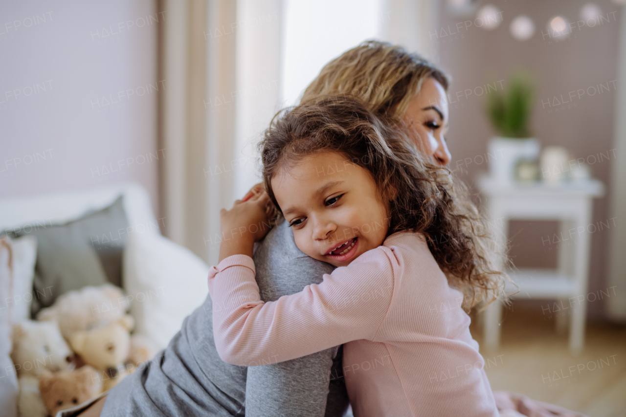 A happy mother with her little daughter hugging together on bed at home.