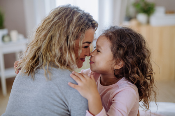 A close-up of happy mother with her little daughter hugging and looking at each other at home.