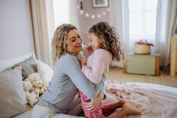 A happy mother with her little daughter hugging and having fun together on bed at home.