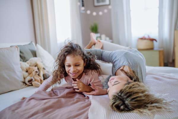 A happy mother with her little daughter hugging and having fun together on bed at home.