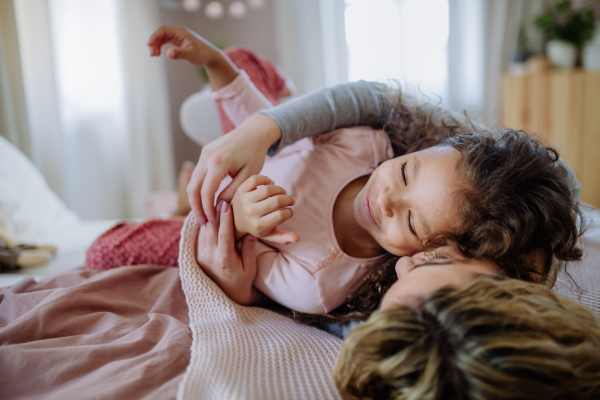 A happy mother with her little daughter hugging and having fun together on bed at home.