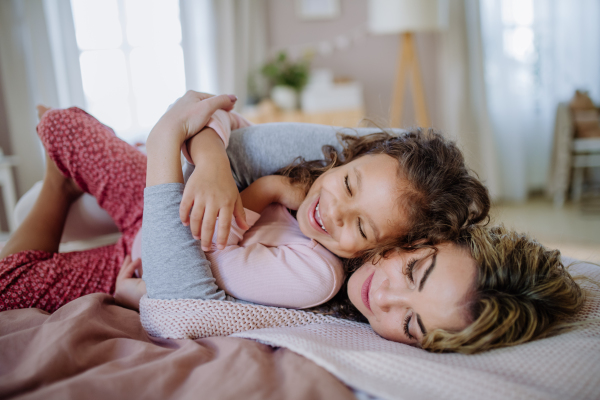 A happy mother lying on bed with her little daughter and cocoonning at home.