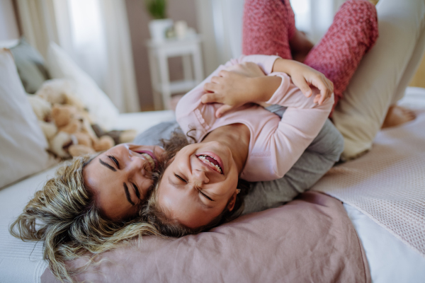 A happy mother with her little daughter hugging and having fun together on bed at home.