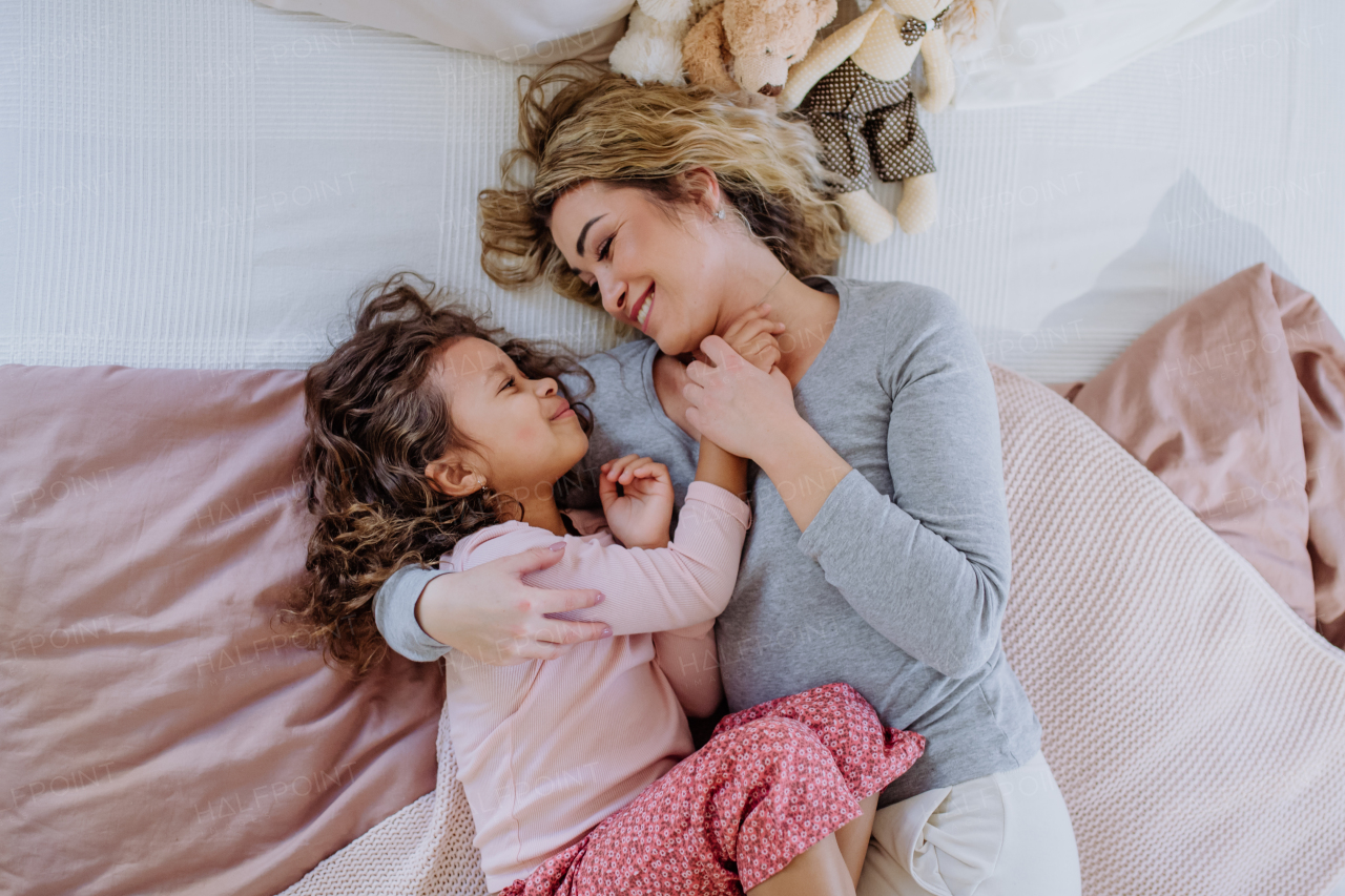 An overhead view of mid adult mother lying on bed with her little daughter at home.