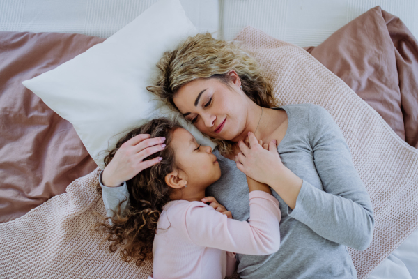 An overhead view of mid adult mother lying on bed with her little daughter at home.