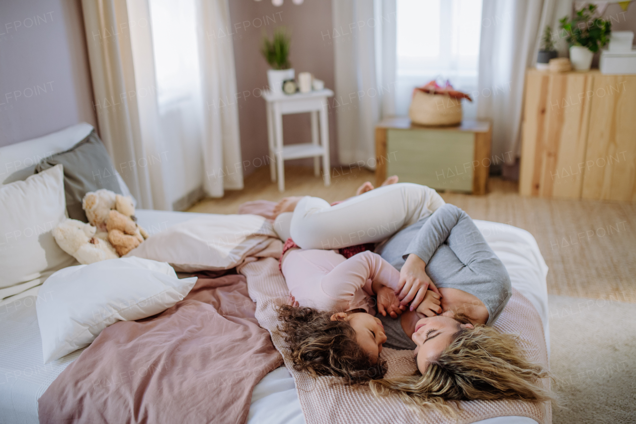 A happy mother with her little daughter lying and looking at each other together on bed at home.