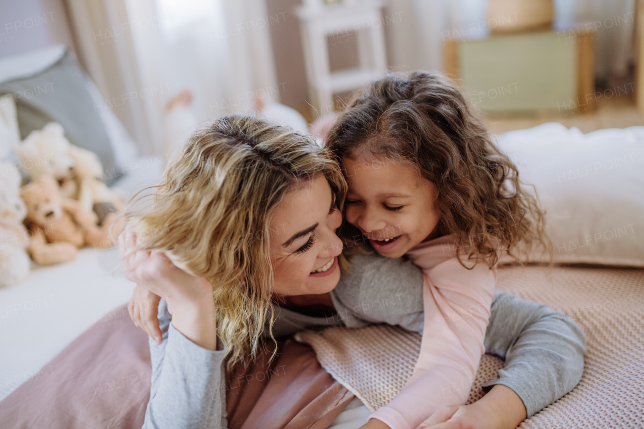 A happy mother with her little daughter hugging and having fun together on bed at home.