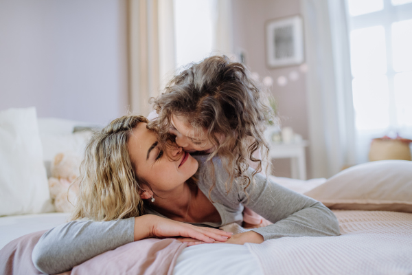 A happy mother with her little daughter hugging and having fun together on bed at home.