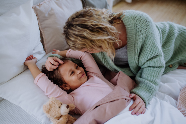 A happy mother stroking her little daughter when waking her up in morning.