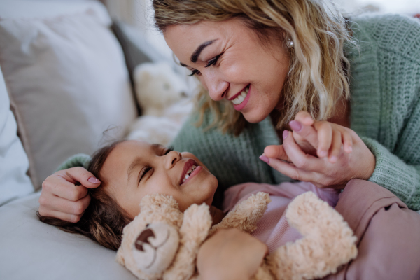 A happy mother stroking her little daughter when looking at each other on bed with her at home.