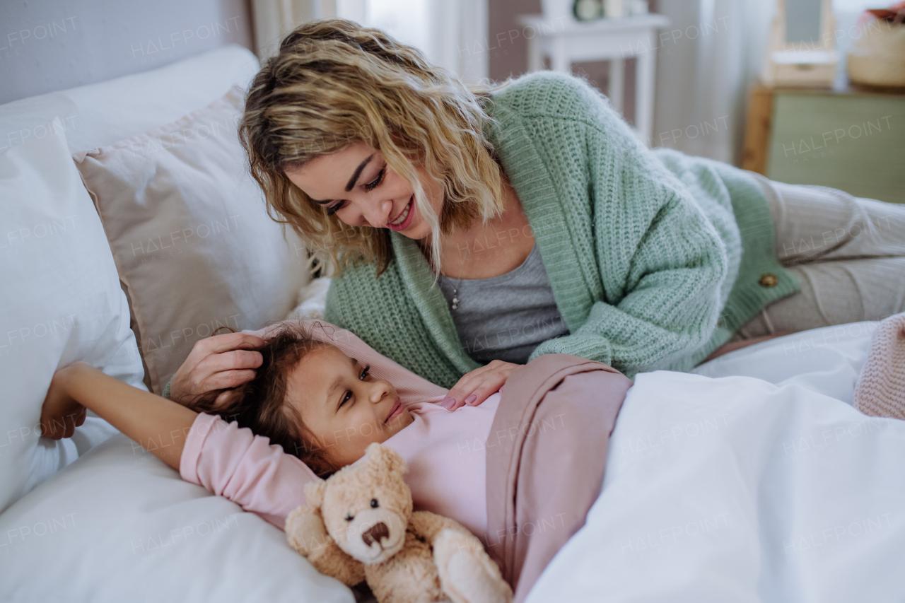 A happy mother stroking her little daughter when looking at each other on bed with her at home.