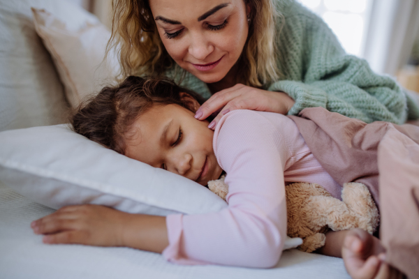 A happy mother stroking her little daughter when waking her up in morning.