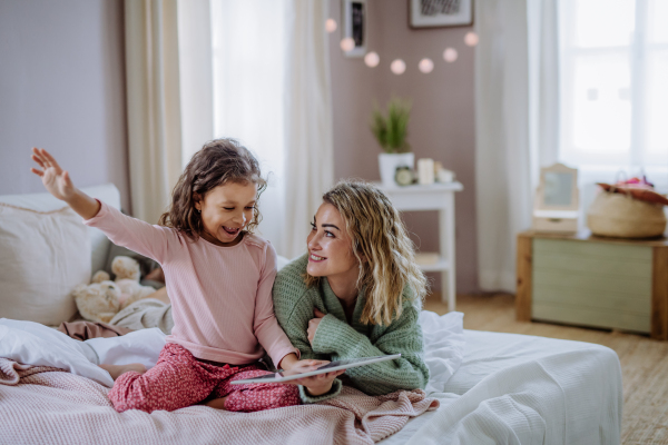 A happy mother with her little daughter lying on bed and using tablet at home.