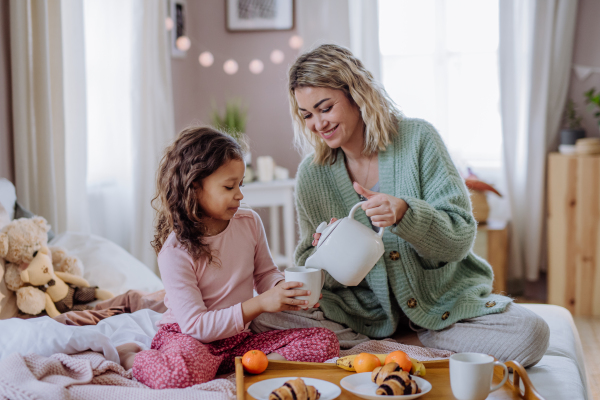 A happy mother with her little daughter having breakfast together in bed at home.