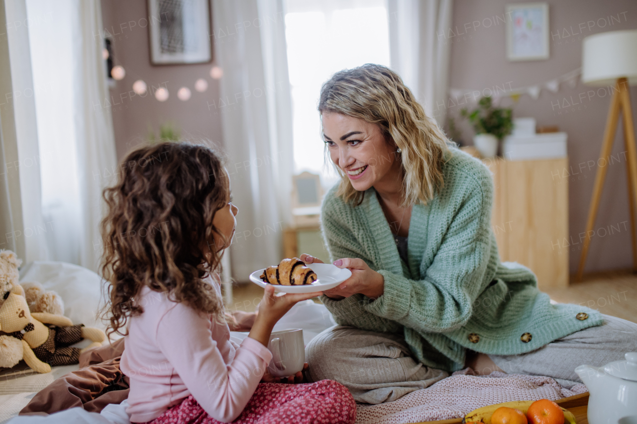 A happy mother with her little daughter having breakfast together in bed at home.