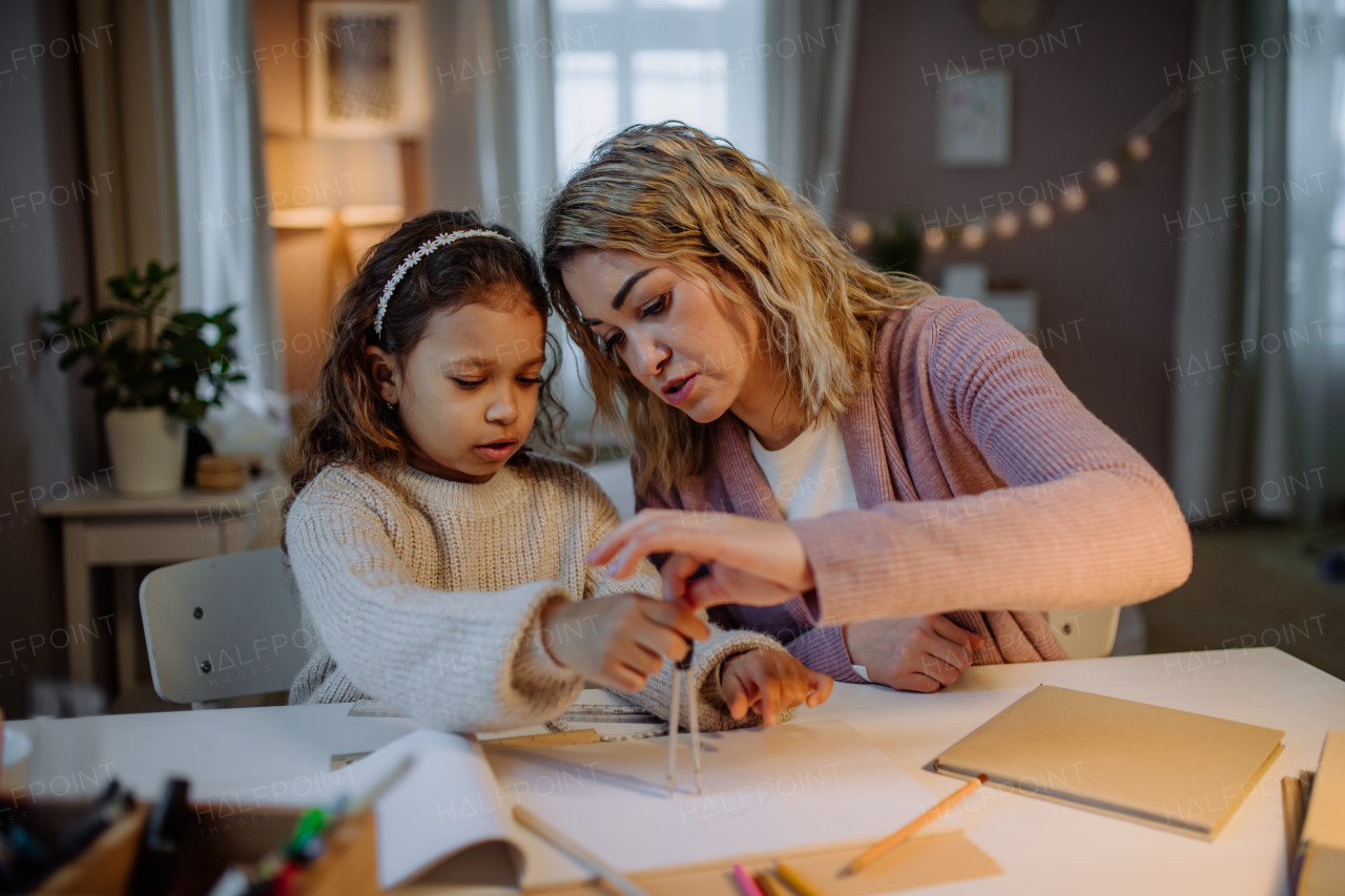 A mother helping her daughter with homework, drawing a circle with comasses in evening at home.