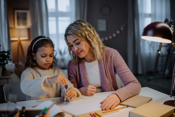 A mother helping her daughter with homework, drawing a circle with comasses in evening at home.