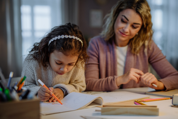 A little girl doing homework with her mother in evening at home.