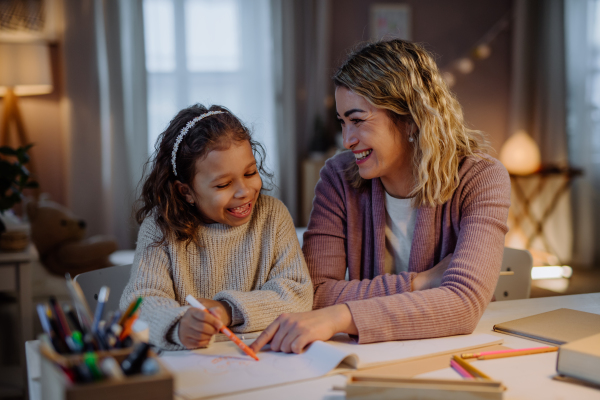 A little girl doing homework with her mother in evening at home.