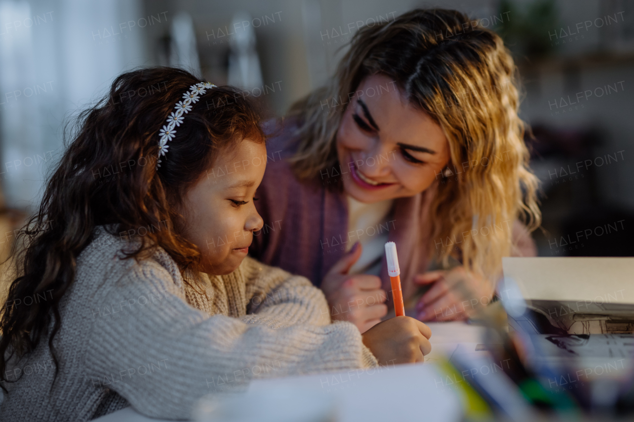 A little girl doing homework with her mother in evening at home.