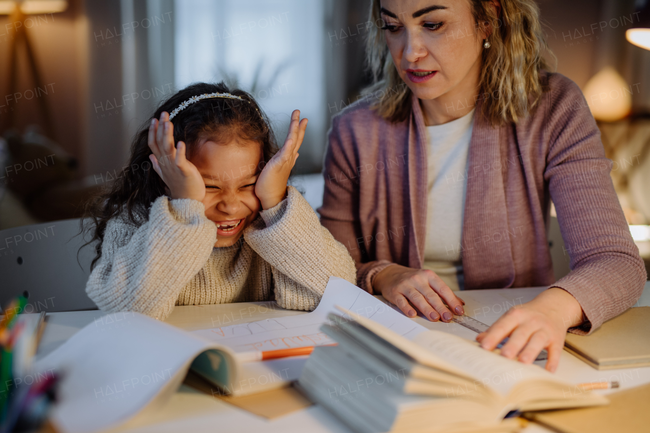 A happy little girl doing homework with her mother in evening at home.