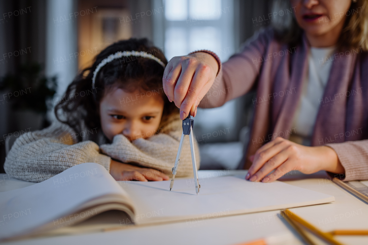 A mother helping her daughter with homework, drawing a circle with comasses in evening at home.