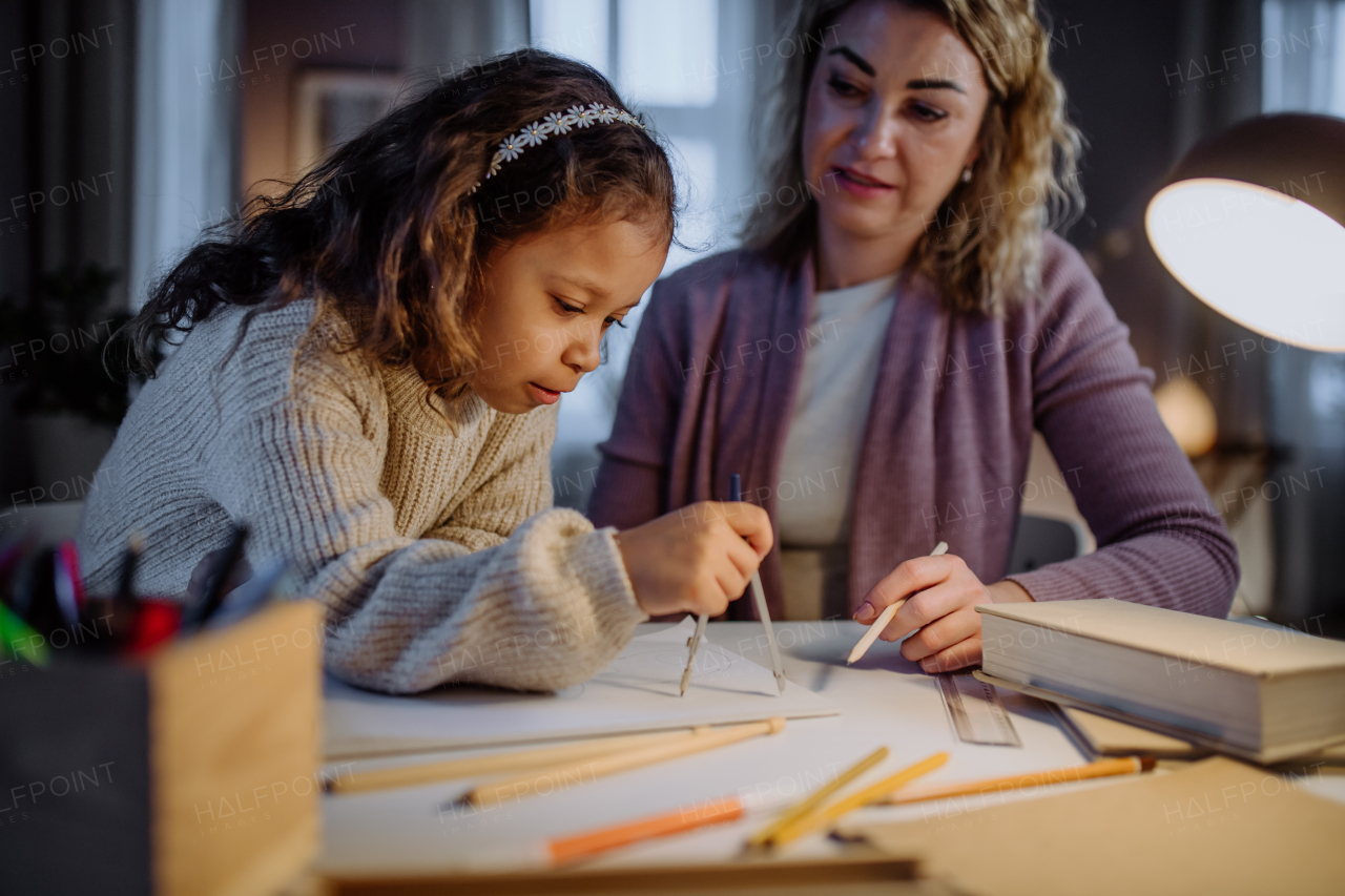 A mother helping her daughter with homework, drawing a circle with comasses in evening at home.