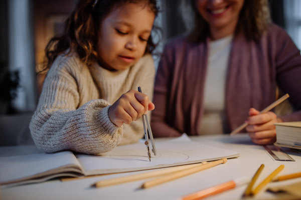 A mother helping her daughter with homework, drawing a circle with comasses in evening at home.