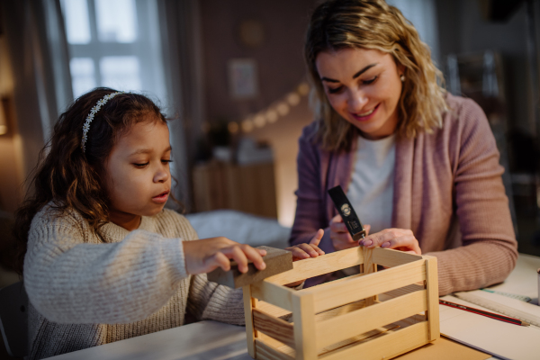 A happy little girl renovating a wooden crate together with her mother at home.