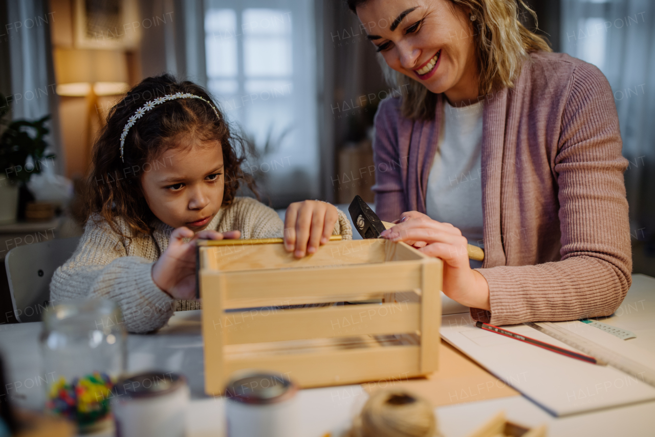 A happy little girl renovating a wooden crate together with her mother at home.