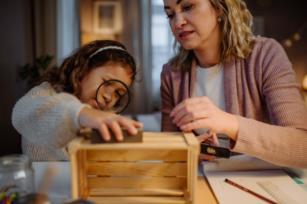 A happy little girl renovating a wooden crate together with her mother at home.