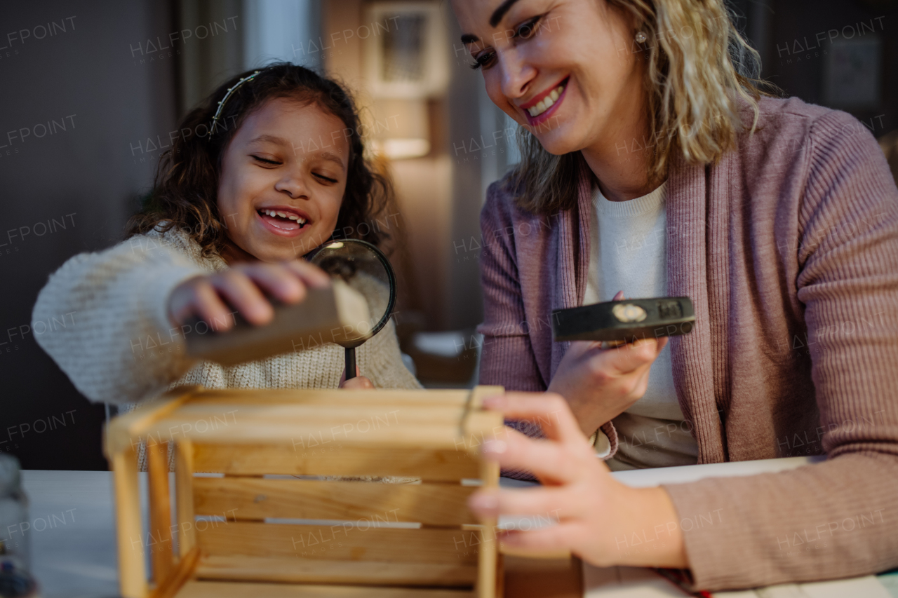 A happy little girl renovating a wooden crate together with her mother at home.