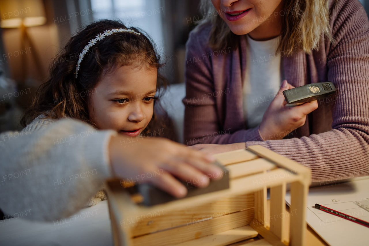 A happy little girl renovating a wooden crate together with her mother at home.