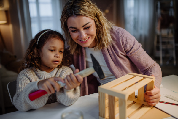 A happy little girl renovating a wooden crate together with her mother at home.