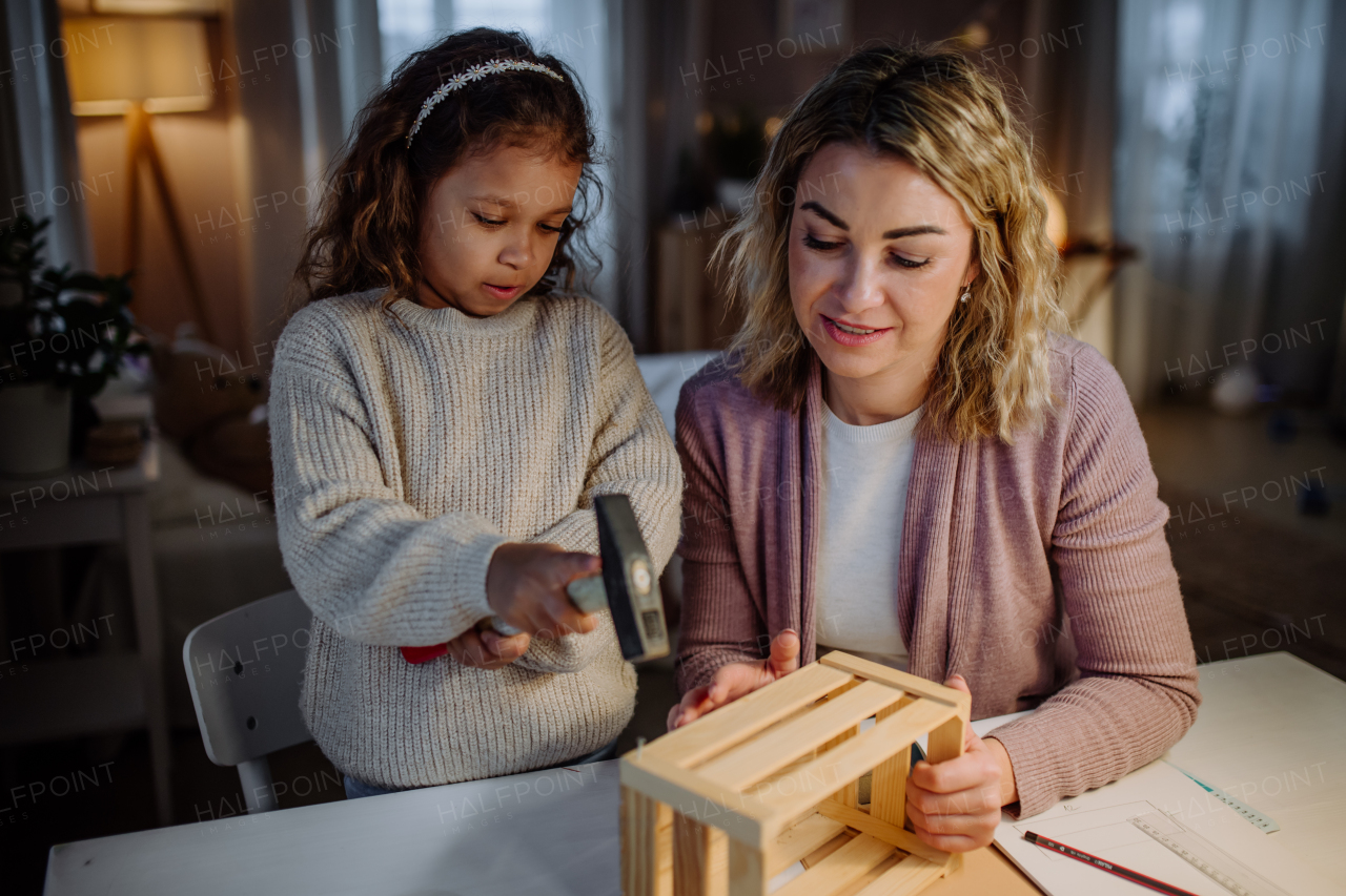 A happy little girl renovating a wooden crate together with her mother at home.