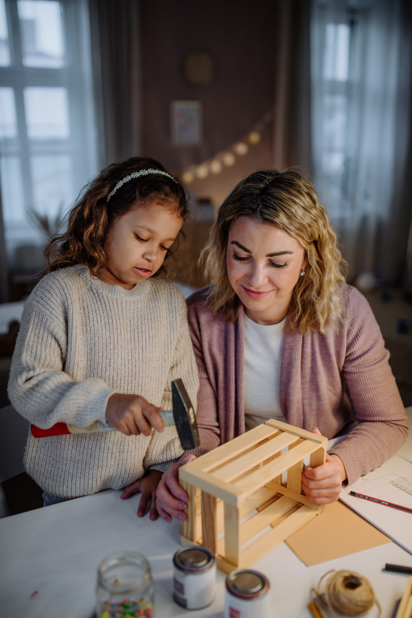 A happy little girl renovating a wooden crate together with her mother at home.