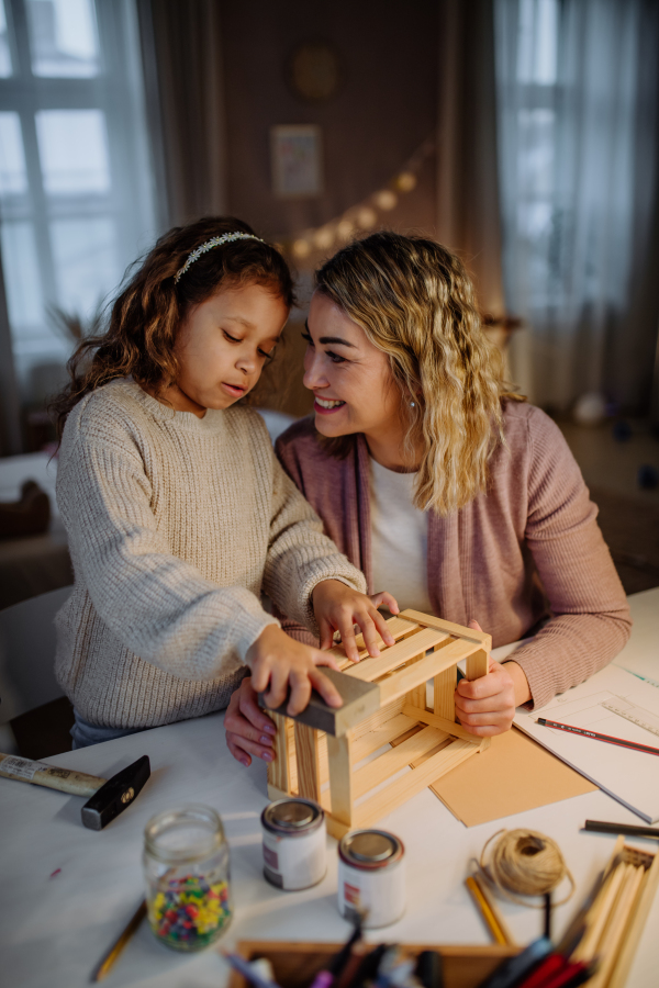 A happy little girl renovating a wooden crate together with her mother at home.