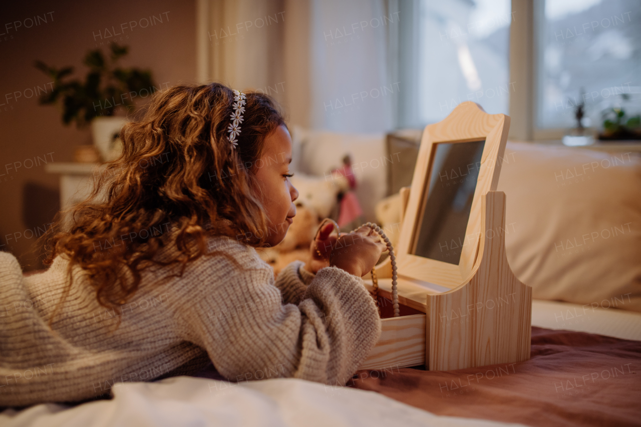 A little multiracial girl lying on bed and looking at her jewlery at home