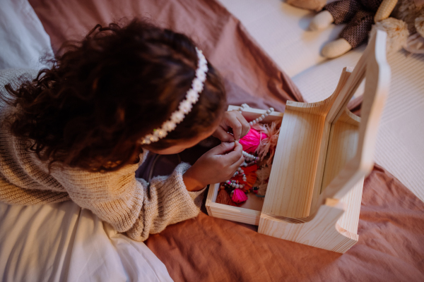 A little multiracial girl lying on bed and looking at her jewlery at home