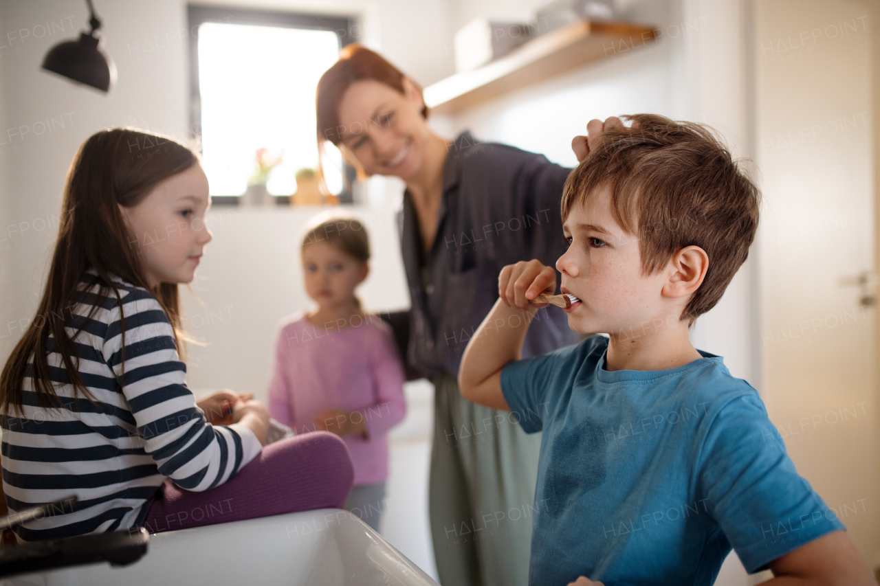 A mother with three little children in bathroom, brushing teeth.