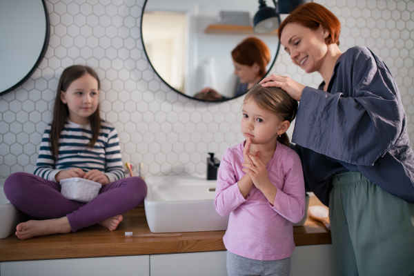 A mother brushing her little daughter's hair in bathroom, morning routine concept.