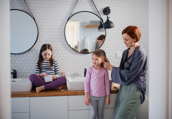 A mother brushing her little daughter's hair in bathroom, morning routine concept.