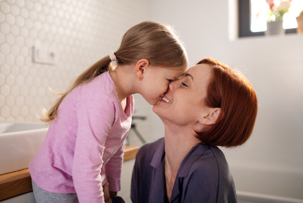 A mother kissing her little daughter in bathroom at home.