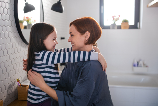 A mother hugging her little daughter in bathroom at home.