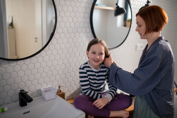 A mother brushing her little daughter's hair in bathroom, morning routine concept.