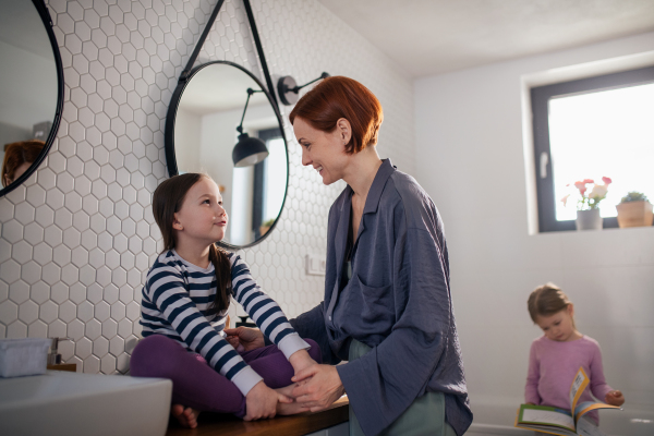 A mother brushing her little daughter's hair and talking in bathroom, morning routine concept.