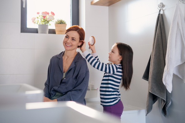 A little girl brushing her mother's hair in bathroom, morning routine concept.