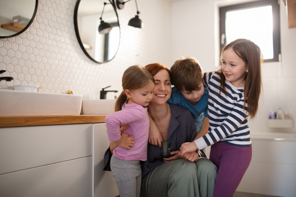 A mother of three little children hugging themr in bathroom at home.