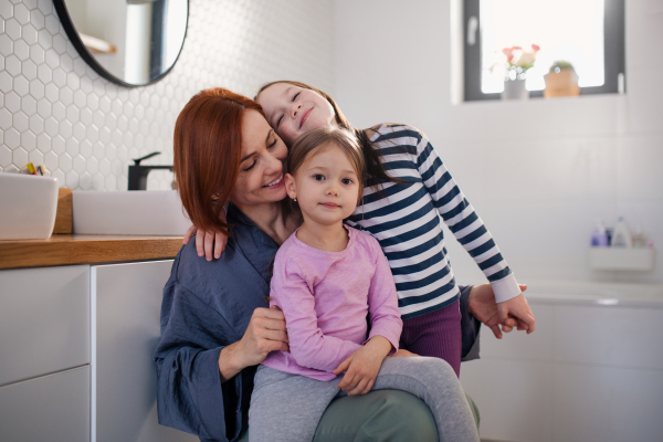 A mother of two little girls hugging them in bathroom at home.